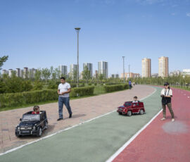 Bambini su macchine giocattolo telecomandate, lungo la pista ciclabile, attraversano il Giardino botanico, Astana, Kazakhstan (© Nick Hannes)